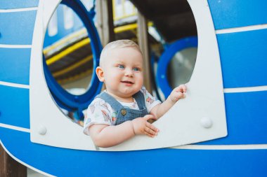 Çocuk parkında gülümseyen 1 yaşında bir çocuk oynuyor. Çocukların açık hava oyun alanı.
