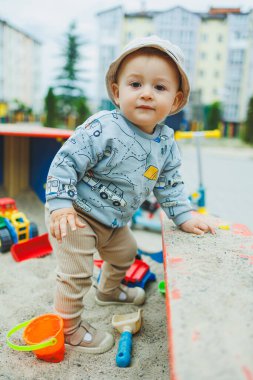 Oyun parkında oturmuş kumla oynayan neşeli bir çocuk. Temiz havada çocuk oyunları oynanıyor. Bebeğin gelişimi..