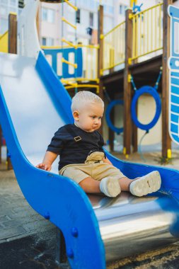1 yaşında bir çocuk oyun parkındaki tepeden aşağı iniyor. Dışarıda bir bebek oynuyor. Çocuk gelişimi.