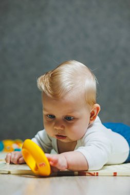 Altı aylık küçük bir çocuk karnının üstüne yatmayı öğreniyor. Bebek yerde oyuncaklarla oynuyor..