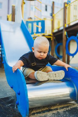 1 yaşında bir çocuk oyun parkındaki tepeden aşağı iniyor. Dışarıda bir bebek oynuyor. Çocuk gelişimi.