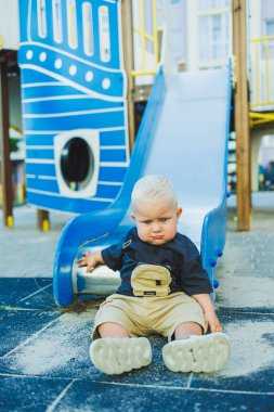 1 yaşında bir çocuk oyun parkındaki tepeden aşağı iniyor. Dışarıda bir bebek oynuyor. Çocuk gelişimi.