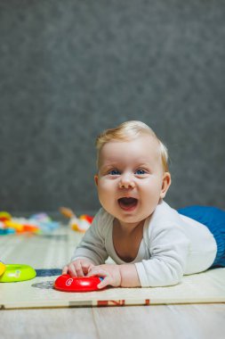 Altı aylık küçük bir çocuk karnının üstüne yatmayı öğreniyor. Bebek yerde oyuncaklarla oynuyor..