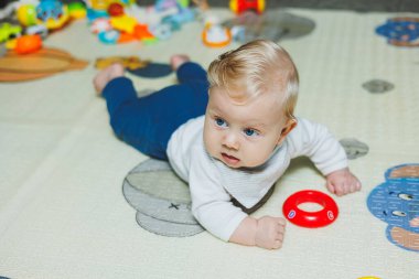 Altı aylık küçük bir çocuk karnının üstüne yatmayı öğreniyor. Bebek yerde oyuncaklarla oynuyor..