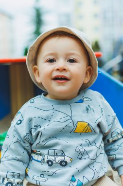 Oyun parkında oturmuş kumla oynayan neşeli bir çocuk. Temiz havada çocuk oyunları oynanıyor. Bebeğin gelişimi..