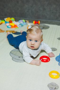 Altı aylık küçük bir çocuk karnının üstüne yatmayı öğreniyor. Bebek yerde oyuncaklarla oynuyor..