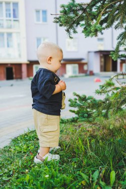 Çocuk parkında açık havada yaz elbisesi giymiş bir çocuk. Bir yaşında bir çocuk, yüksek binaların yakınındaki modern bir avluda yürüyor. Çok katlı bir binada çocuk parkı.