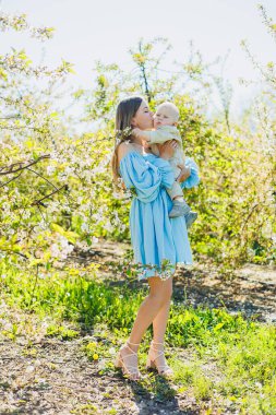 Genç ve mutlu bir anne doğada dururken küçük oğlunu kollarına alır. Bir çocukla yürüyüş. Anne bir bebekle yürüyüşe çıktı..