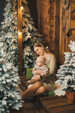 Yeni yıl tatili için dekore edilmiş bir odada kollarında mutlu bir anne ve küçük bir oğul. Aile geleneği.