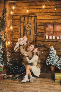 Genç anne ve baba evdeki Noel ağacının yanında otururken çocuklarıyla oynuyorlar. Noel aile ortamı