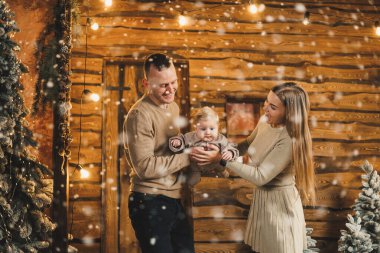 Şefkatli bir çift güzel bir Noel ağacının yanında oturuyor ve oğullarının şık örgü elbiseleriyle eğleniyorlar. Kış tatilinde mutlu aile anları.