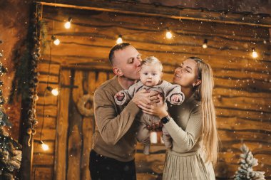 Şefkatli bir çift güzel bir Noel ağacının yanında oturuyor ve oğullarının şık örgü elbiseleriyle eğleniyorlar. Kış tatilinde mutlu aile anları.