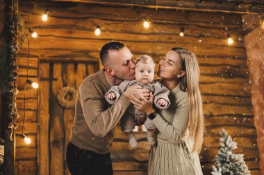 Şefkatli bir çift güzel bir Noel ağacının yanında oturuyor ve oğullarının şık örgü elbiseleriyle eğleniyorlar. Kış tatilinde mutlu aile anları.