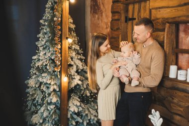 Şefkatli bir çift güzel bir Noel ağacının yanında oturuyor ve oğullarının şık örgü elbiseleriyle eğleniyorlar. Kış tatilinde mutlu aile anları.