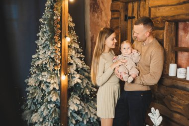 Şefkatli bir çift güzel bir Noel ağacının yanında oturuyor ve oğullarının şık örgü elbiseleriyle eğleniyorlar. Kış tatilinde mutlu aile anları.