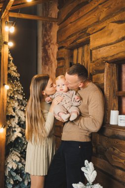 Şefkatli bir çift güzel bir Noel ağacının yanında oturuyor ve oğullarının şık örgü elbiseleriyle eğleniyorlar. Kış tatilinde mutlu aile anları.