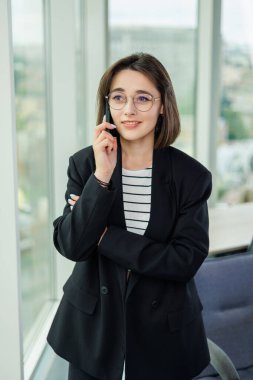 Geniş bir ofiste çalışan genç bir kadın telefonda konuşuyor. Başarılı insanlar yeni bir iş projesi üzerinde çalışıyorlar. Ofiste toplu iş var.