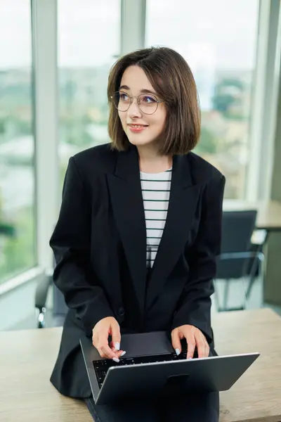 stock image Woman business manager smiling working on laptop in office. An employee works in an office with large windows.