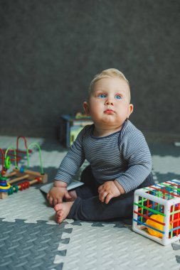 Bir bebek evde yerde oturuyor ve oyuncaklarla oynuyor. Bebekler için eğitici oyuncaklar. Pamuk elbiseli bir çocuk..