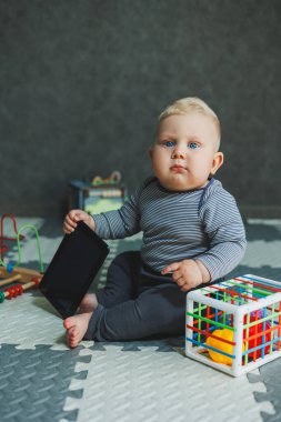 Bir bebek evde yerde oturuyor ve oyuncaklarla oynuyor. Bebekler için eğitici oyuncaklar. Pamuk elbiseli bir çocuk..