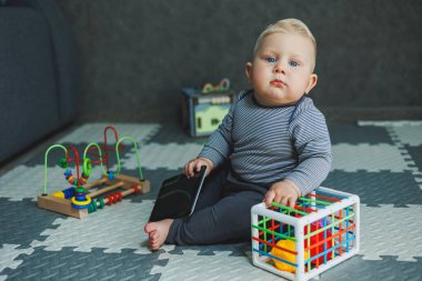 Bir bebek evde yerde oturuyor ve oyuncaklarla oynuyor. Bebekler için eğitici oyuncaklar. Pamuk elbiseli bir çocuk..