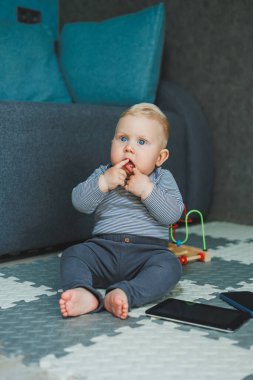 Bir bebek evde yerde oturuyor ve oyuncaklarla oynuyor. Bebekler için eğitici oyuncaklar. Pamuk elbiseli bir çocuk..