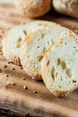 Koyu beton zeminde ahşap bir tahtada dilimlenmiş taze zanaat ekmeği. Ev yapımı pişirme.