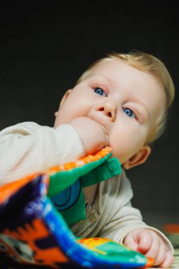 Evde bebek oyuncaklarıyla oynayan tatlı sarışın çocuk oturma odasında halının üzerinde oturuyor. Gülümseyen küçük sevimli çocuk renkli oyuncaklar kullanıyor, ip çiğniyor.