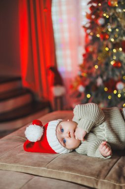 Noel Baba şapkalı bir çocuk Noel ağacının arka planında. Örgü kazak giyen bir bebek..