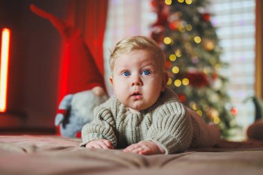 Noel ağacı oyuncaklarıyla arka planda sevimli bir erkek bebek, geleneksel Noel kostümü. Yeni yıl tatili. Bir bebek için ilk yeni yıl