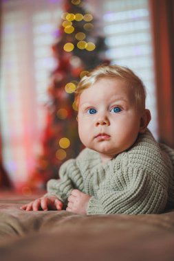 Noel ağacı oyuncaklarıyla arka planda sevimli bir erkek bebek, geleneksel Noel kostümü. Yeni yıl tatili. Bir bebek için ilk yeni yıl