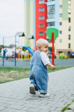 Kot pantolon giymiş, 1 yaşında bir erkek bebek sokakta yürüyor. Büyük boy çocuk tulumu. Çocuk parkında şık küçük bir çocuk.