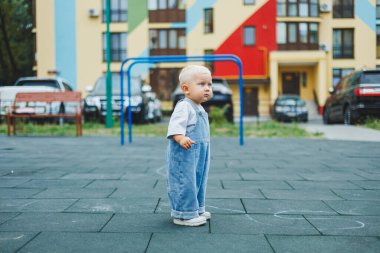 Kot pantolon giymiş, 1 yaşında bir erkek bebek sokakta yürüyor. Büyük boy çocuk tulumu. Çocuk parkında şık küçük bir çocuk.