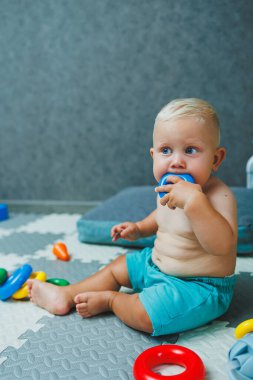 Şortlu küçük bir çocuk evde halıya oturup eğitici oyuncaklarla oynuyor. Bir çocuk plastik piramit inşa eder..