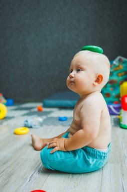 Şortlu küçük bir çocuk evde halıya oturup eğitici oyuncaklarla oynuyor. Bir çocuk plastik piramit inşa eder..