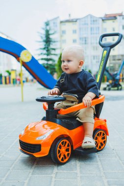 Küçük bir çocuk, 1 yaşında, plastik bir arabada oturuyor. Bebekleri besleyen bir makine. Çocuklar için Tolokar.