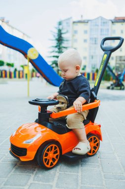 Küçük bir çocuk, 1 yaşında, plastik bir arabada oturuyor. Bebekleri besleyen bir makine. Çocuklar için Tolokar.