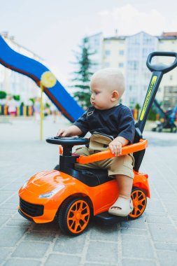 Küçük bir çocuk, 1 yaşında, plastik bir arabada oturuyor. Bebekleri besleyen bir makine. Çocuklar için Tolokar.