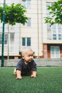 Parktaki stadyumda koşan neşeli 1 yaşında bir çocuk. Yeşil çim tarlası. Çocuğun aktif yaşam tarzı bu. Bir bebek için sağlıklı bir yaşam tarzı. Bir erkek için şık kıyafetler..