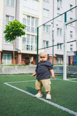 Parktaki stadyumda koşan neşeli 1 yaşında bir çocuk. Yeşil çim tarlası. Çocuğun aktif yaşam tarzı bu. Bir bebek için sağlıklı bir yaşam tarzı. Bir erkek için şık kıyafetler..