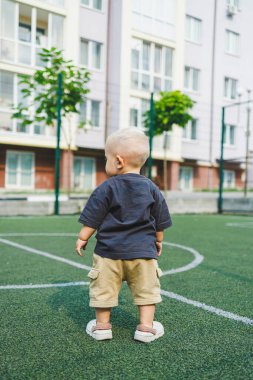 Parktaki stadyumda koşan neşeli 1 yaşında bir çocuk. Yeşil çim tarlası. Çocuğun aktif yaşam tarzı bu. Bir bebek için sağlıklı bir yaşam tarzı. Bir erkek için şık kıyafetler..