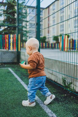 Sokakta kot pantolon ve tişört giyen küçük bir çocuk oynuyor. Erkekler için Denim giysileri. Spor sahasında bir çocuk. Çocuk gelişimi.