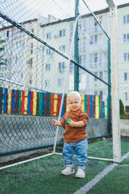 Sokakta kot pantolon ve tişört giyen küçük bir çocuk oynuyor. Erkekler için Denim giysileri. Spor sahasında bir çocuk. Çocuk gelişimi.