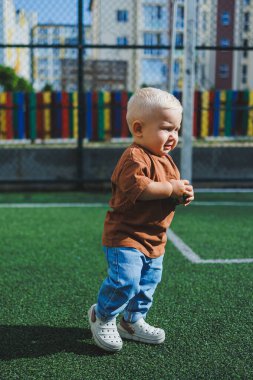 Sokakta kot pantolon ve tişört giyen küçük bir çocuk oynuyor. Erkekler için Denim giysileri. Spor sahasında bir çocuk. Çocuk gelişimi.