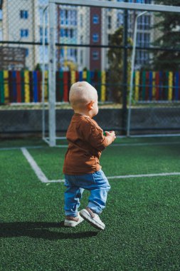 Sokakta kot pantolon ve tişört giyen küçük bir çocuk oynuyor. Erkekler için Denim giysileri. Spor sahasında bir çocuk. Çocuk gelişimi.