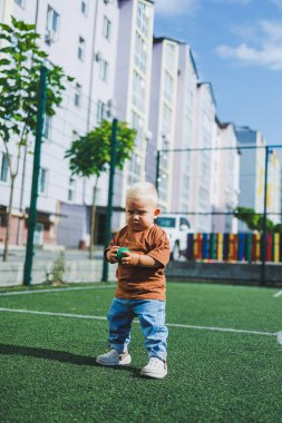 Sokakta şık bir kot pantolon ve tişört giyen 1 yaşında bir çocuk oynuyor. Bir çocuk oyun parkında dışarıda oynuyor. Futbol sahasında bir çocuk.