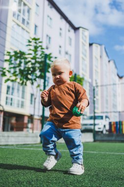 Sokakta şık bir kot pantolon ve tişört giyen 1 yaşında bir çocuk oynuyor. Bir çocuk oyun parkında dışarıda oynuyor. Futbol sahasında bir çocuk.
