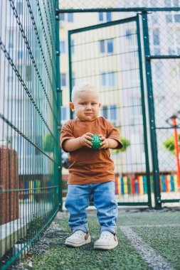 Sokakta şık bir kot pantolon ve tişört giyen 1 yaşında bir çocuk oynuyor. Bir çocuk oyun parkında dışarıda oynuyor. Futbol sahasında bir çocuk.