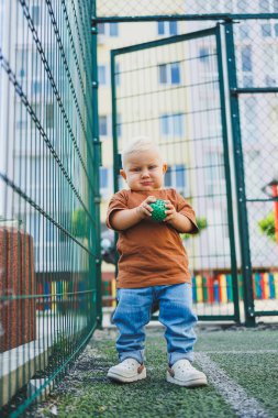 Sokakta şık bir kot pantolon ve tişört giyen 1 yaşında bir çocuk oynuyor. Bir çocuk oyun parkında dışarıda oynuyor. Futbol sahasında bir çocuk.