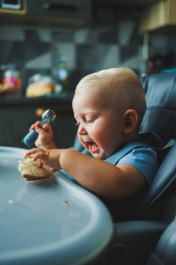 1 yaşında bir çocuk yüksek bir sandalyede oturur ve ekmek yer. Bebek ekmek yiyor. Çocuğun kendi kendini beslemesi..